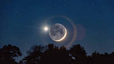 Открытая книга по астрологии и две распечатанные натальные карты на столе у окна вечером.