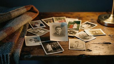 Россыпь старых семейных фотографий на деревянном столе в тёплом вечернем свете лампы