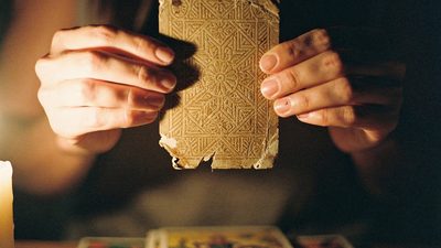 Расклад таро на отношения, женские руки держат карту таро рубашкой вверх в тёплом свете