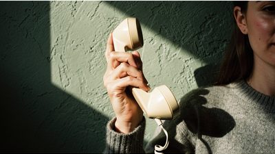 Женские руки держат у уха старую дисковую телефонную трубку в спокойном дневном свете