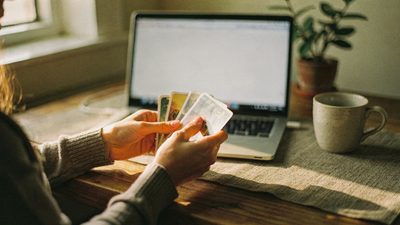 Девушка учится работать тарологом онлайн, раскладывает карты таро у ноутбука для консультации