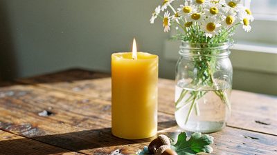 Жёлтая свеча, банка с ромашками и веточка дуба на столе у окна в светлый вечер солнцестояния